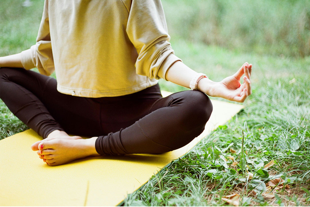 Person sitzt auf einer Yogamatte auf dem Gras im Lotussitz