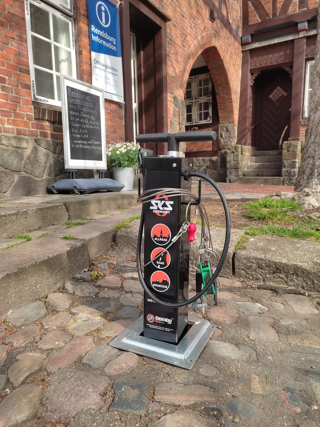 Eine mobile Fahrradstation mit verschiedenen Werkzeugen und einer Standluftpumpe steht vor dem Eingang zur Touristeninformation.